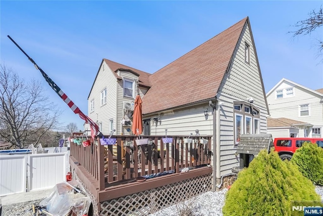 rear view of property with a shingled roof, fence, and a wooden deck