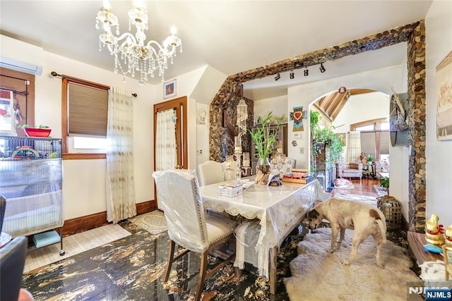 dining space with an inviting chandelier, a wall unit AC, baseboards, and arched walkways