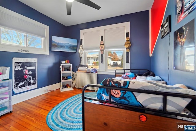 bedroom featuring multiple windows, radiator, baseboards, and wood finished floors