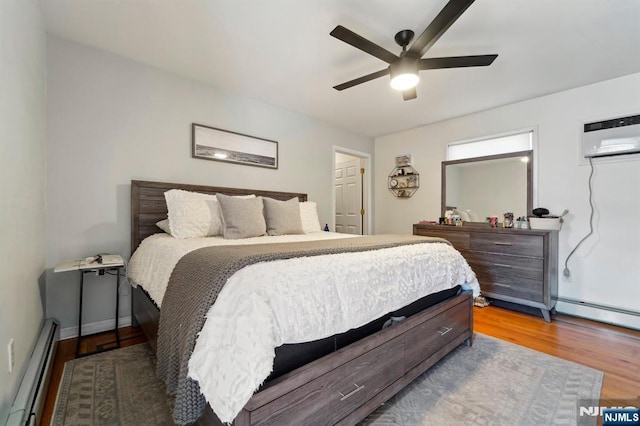 bedroom featuring wood finished floors, ceiling fan, an AC wall unit, a baseboard heating unit, and baseboard heating