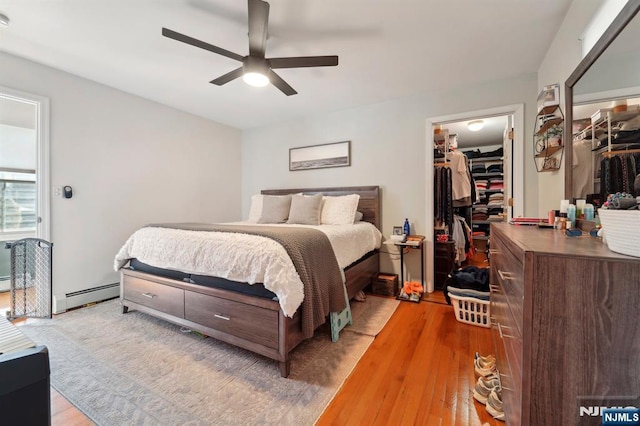 bedroom with a spacious closet, ceiling fan, light wood-style floors, a closet, and a baseboard radiator