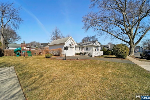 exterior space with a playground, fence, concrete driveway, a lawn, and an attached garage