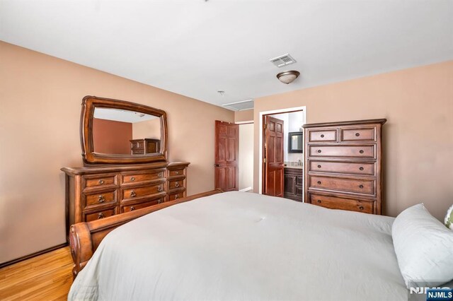 bedroom with visible vents, light wood-style floors, and connected bathroom