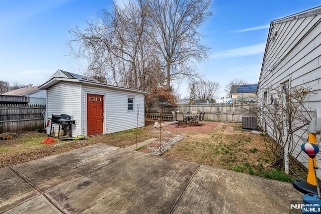 view of yard with a fenced backyard, central air condition unit, an outbuilding, and a patio