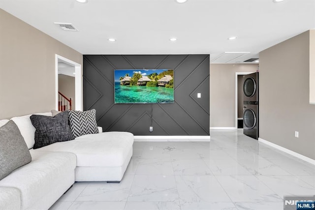 unfurnished living room featuring baseboards, marble finish floor, stacked washer and clothes dryer, and an accent wall