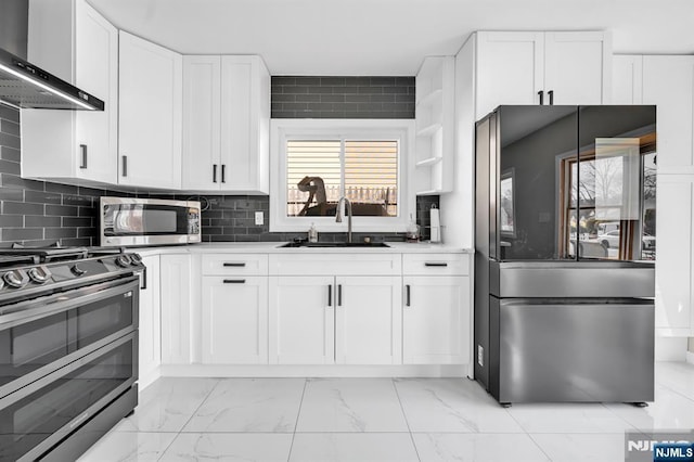 kitchen featuring marble finish floor, a sink, backsplash, appliances with stainless steel finishes, and wall chimney range hood