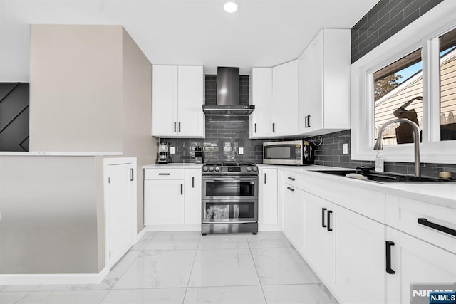 kitchen with a sink, light countertops, appliances with stainless steel finishes, wall chimney exhaust hood, and marble finish floor