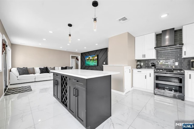 kitchen featuring wall chimney range hood, double oven range, decorative backsplash, marble finish floor, and white cabinetry