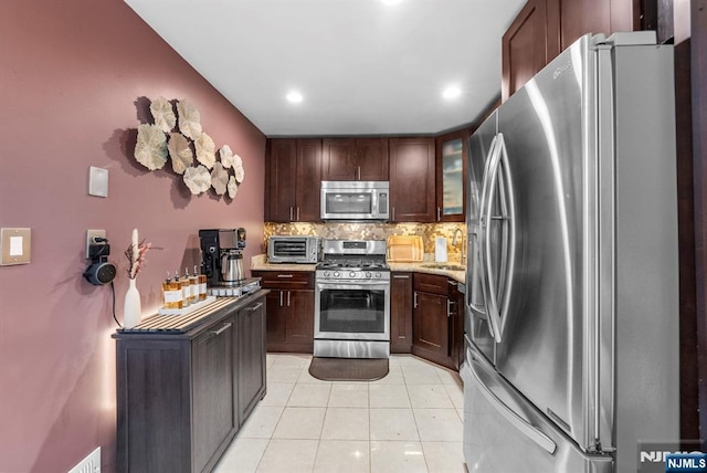 kitchen with dark brown cabinets, tasteful backsplash, appliances with stainless steel finishes, and light tile patterned flooring