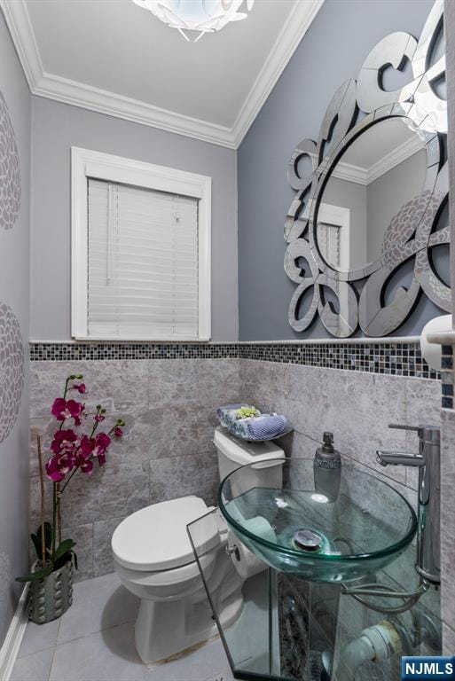 bathroom featuring tile patterned flooring, crown molding, toilet, wainscoting, and tile walls