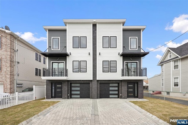 view of front of house featuring a balcony, fence, brick siding, and driveway