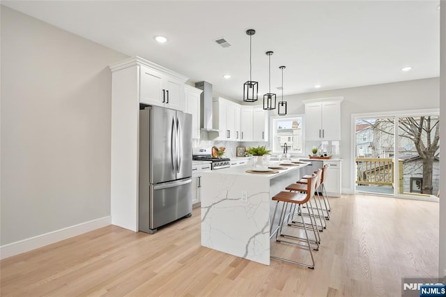 kitchen featuring backsplash, a kitchen bar, freestanding refrigerator, stove, and wall chimney exhaust hood