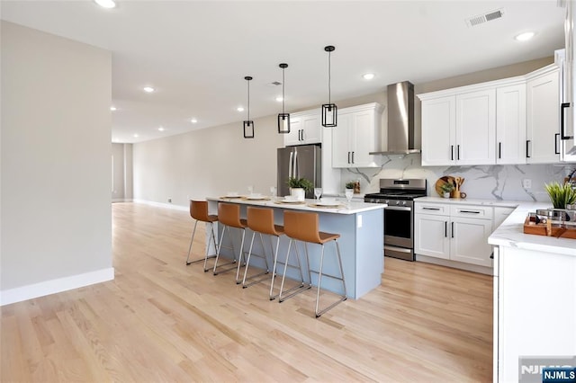 kitchen with backsplash, a kitchen island, a breakfast bar, appliances with stainless steel finishes, and wall chimney exhaust hood