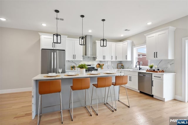 kitchen with stainless steel appliances, white cabinets, a kitchen bar, wall chimney range hood, and a center island