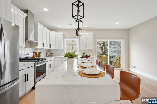 kitchen featuring tasteful backsplash, visible vents, a kitchen island, wall chimney range hood, and appliances with stainless steel finishes