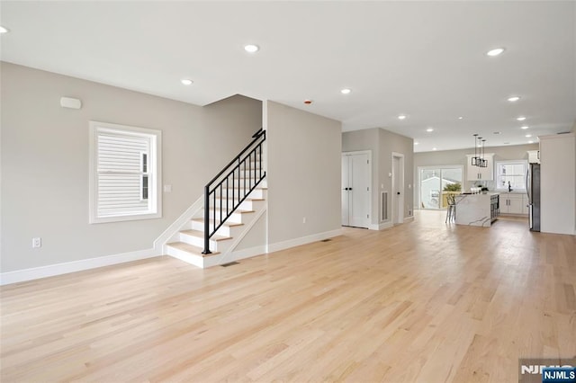 unfurnished living room featuring recessed lighting, stairway, light wood-style flooring, and baseboards