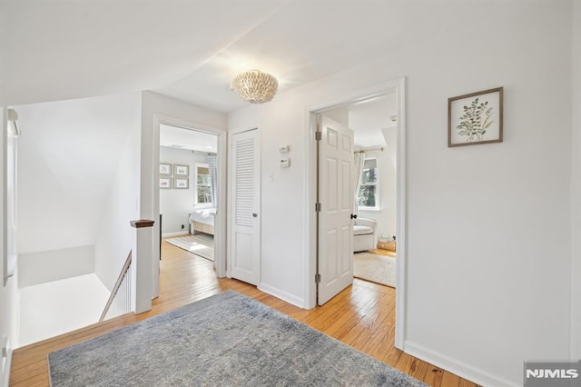 corridor with baseboards, light wood-type flooring, an upstairs landing, and a healthy amount of sunlight