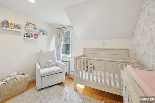 bedroom featuring a nursery area, wood finished floors, radiator heating unit, and vaulted ceiling