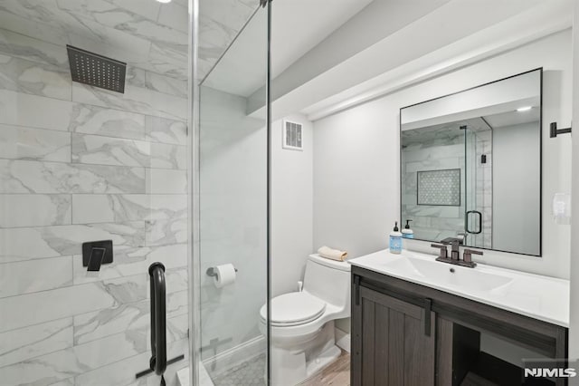 bathroom featuring visible vents, toilet, a shower stall, baseboards, and vanity