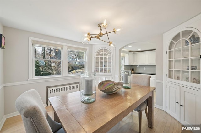 dining room with arched walkways, light wood-style floors, a chandelier, and radiator heating unit