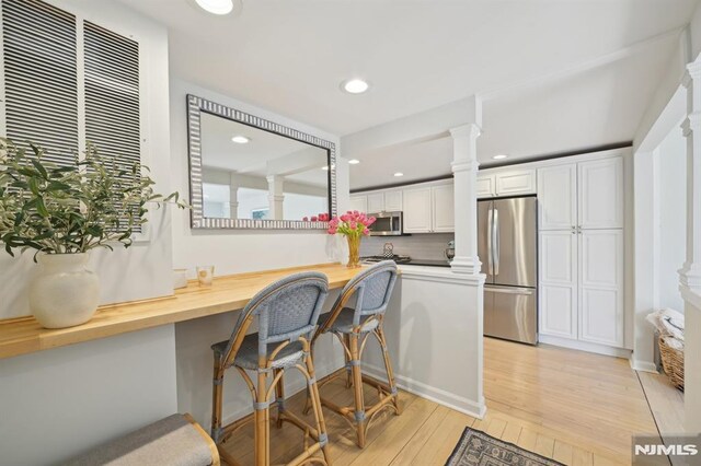 kitchen featuring ornate columns, stainless steel appliances, white cabinetry, a kitchen breakfast bar, and light wood-type flooring