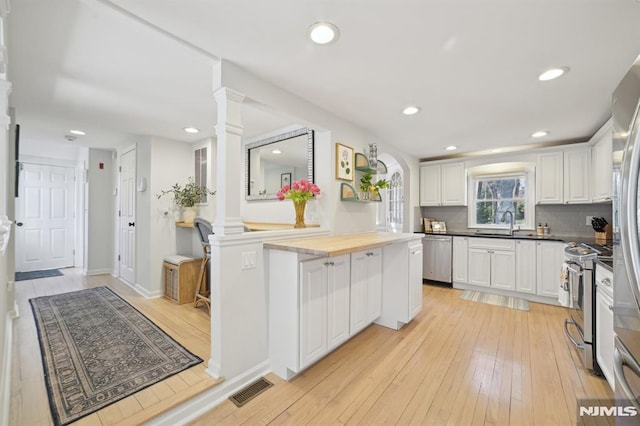 kitchen with stainless steel appliances, white cabinetry, light wood-style floors, and ornate columns