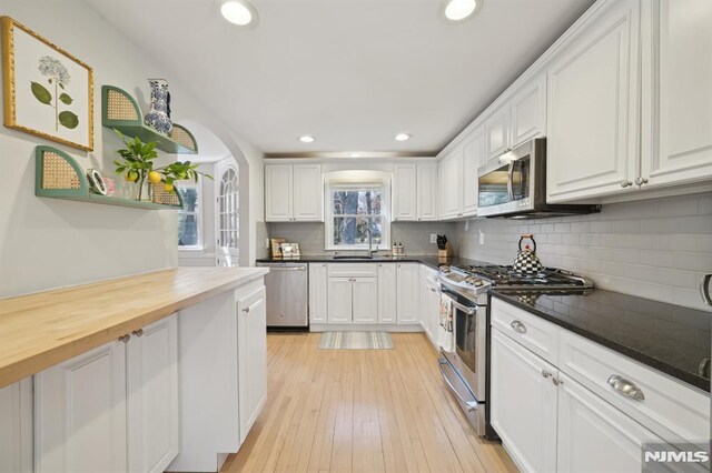 kitchen with light wood-type flooring, a sink, tasteful backsplash, stainless steel appliances, and white cabinets