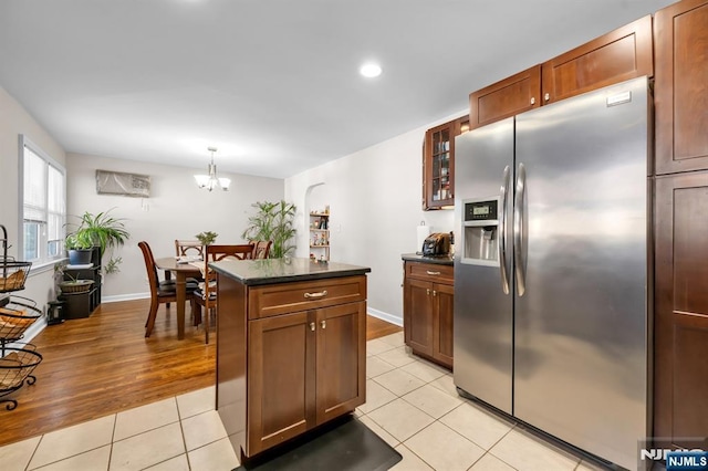 kitchen with dark countertops, a kitchen island, glass insert cabinets, light tile patterned floors, and stainless steel refrigerator with ice dispenser