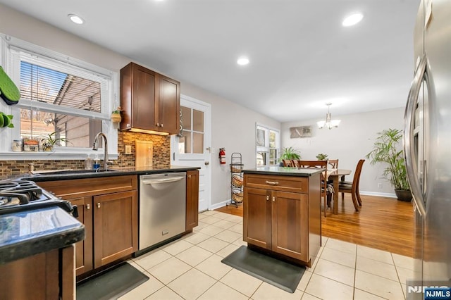 kitchen featuring a sink, backsplash, dark countertops, appliances with stainless steel finishes, and light tile patterned floors