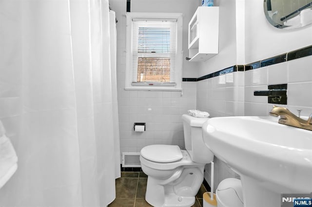 full bathroom featuring tile patterned flooring, tile walls, toilet, and a sink