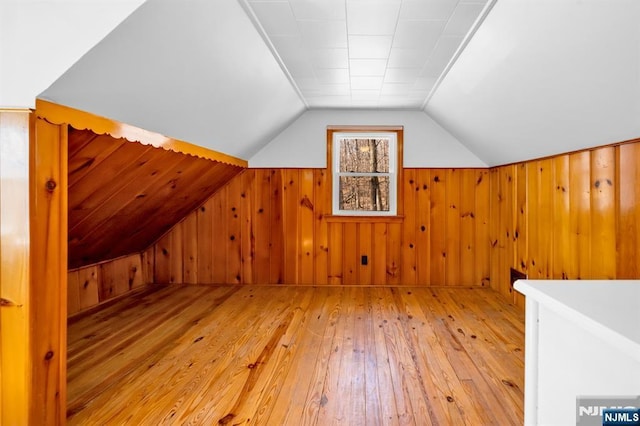 bonus room with lofted ceiling, wooden walls, and light wood finished floors