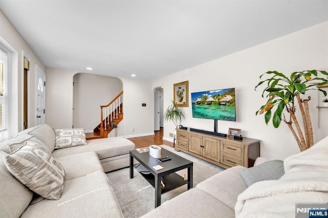 living room with light wood-style flooring, recessed lighting, arched walkways, baseboards, and stairs