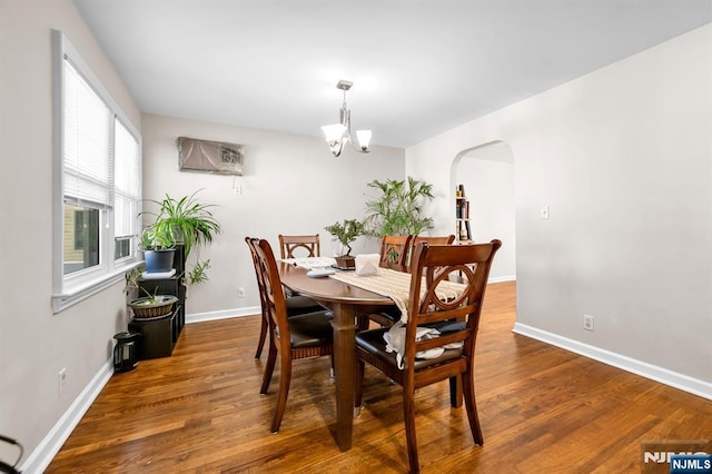 dining room with a chandelier, arched walkways, baseboards, and wood finished floors