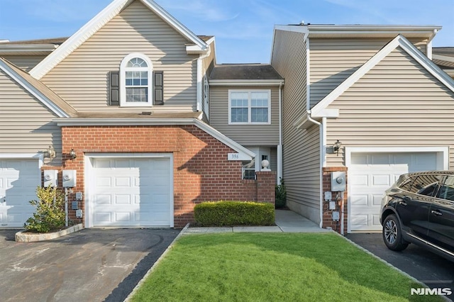 view of front facade featuring aphalt driveway, an attached garage, brick siding, and a front yard