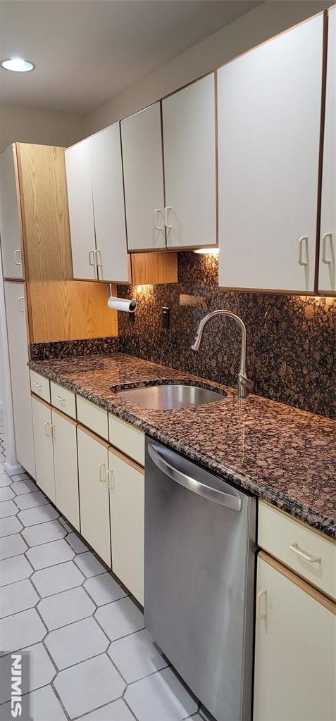 kitchen featuring dark stone countertops, a sink, white cabinets, dishwasher, and backsplash