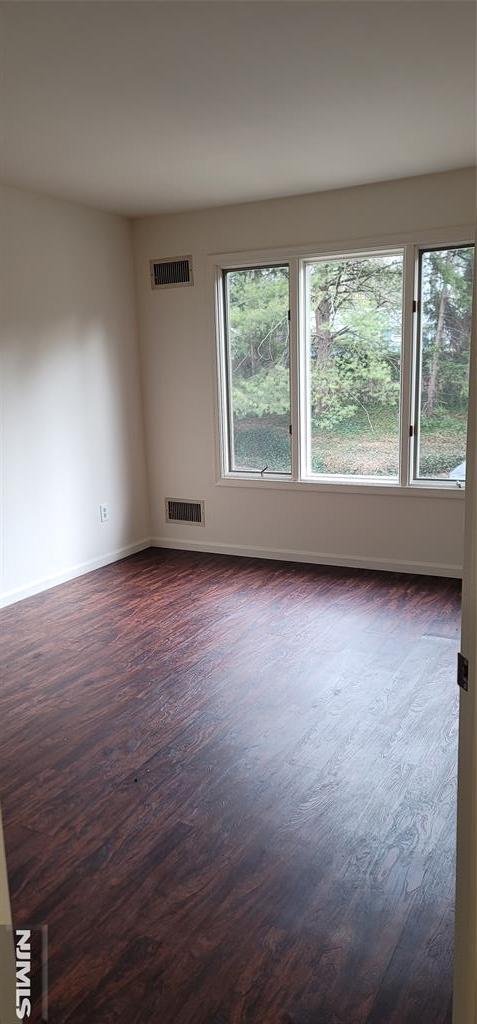 spare room with dark wood finished floors, visible vents, and baseboards