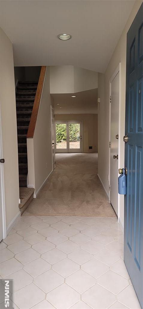 hallway with stairway, baseboards, light colored carpet, and vaulted ceiling