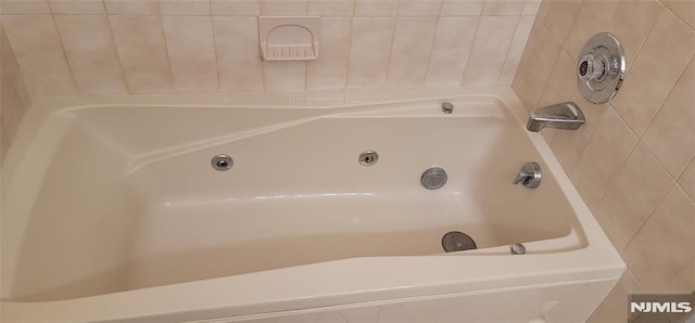 bathroom with a tub with jets and tile walls