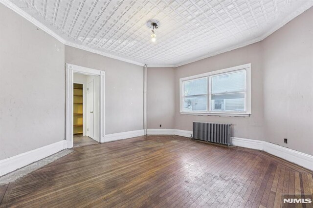 empty room with baseboards, radiator heating unit, ornamental molding, an ornate ceiling, and wood-type flooring