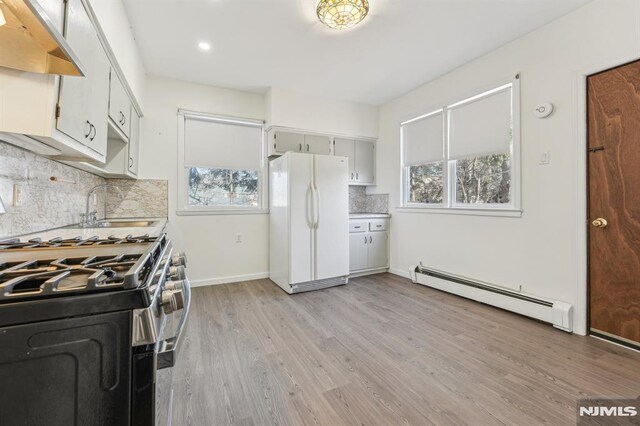 kitchen with under cabinet range hood, a sink, gas range oven, freestanding refrigerator, and baseboard heating