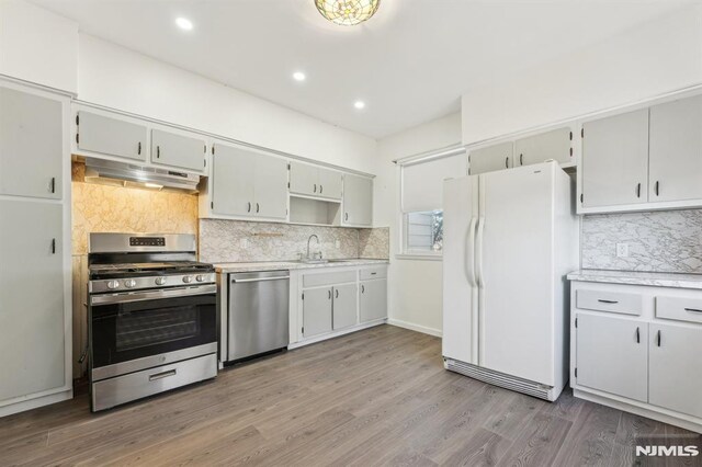 kitchen featuring under cabinet range hood, a sink, wood finished floors, appliances with stainless steel finishes, and light countertops