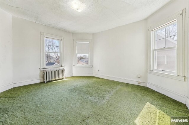 unfurnished room featuring radiator, a textured ceiling, baseboards, and carpet floors