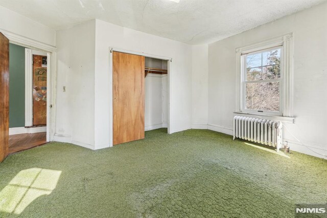 unfurnished bedroom with a textured ceiling, radiator heating unit, a closet, carpet floors, and baseboards