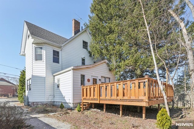 back of property featuring a wooden deck, roof with shingles, and a chimney