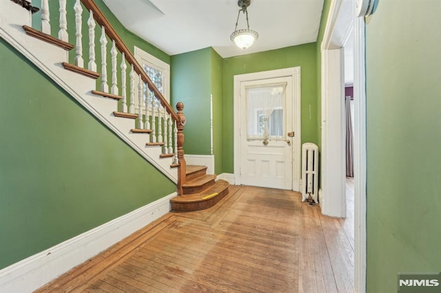 foyer entrance featuring hardwood / wood-style floors, stairway, radiator heating unit, and baseboards