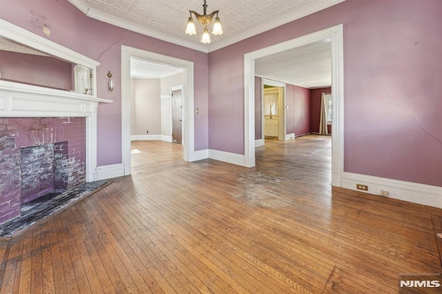 unfurnished living room with a brick fireplace, baseboards, a chandelier, ornamental molding, and hardwood / wood-style flooring