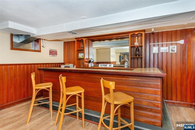 bar featuring a wainscoted wall, a textured ceiling, light wood-style floors, a bar, and wood walls