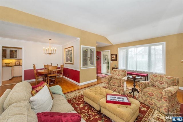 living room with an inviting chandelier, vaulted ceiling, wood finished floors, and baseboards