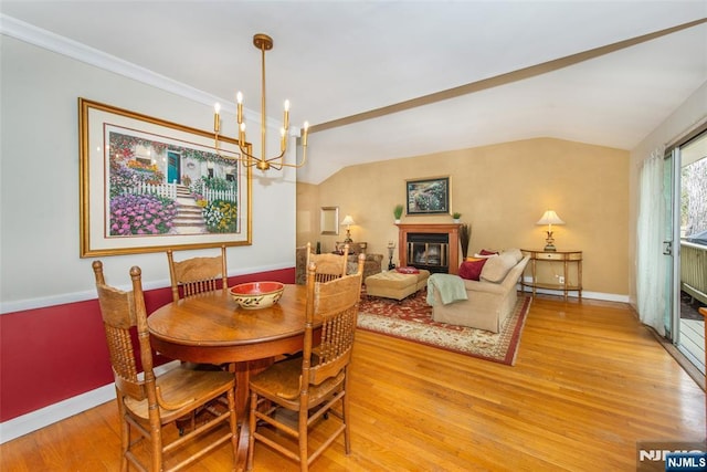 dining area with a glass covered fireplace, lofted ceiling, baseboards, and light wood finished floors