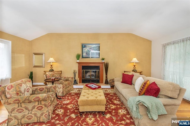 living area with a glass covered fireplace, wood finished floors, and vaulted ceiling